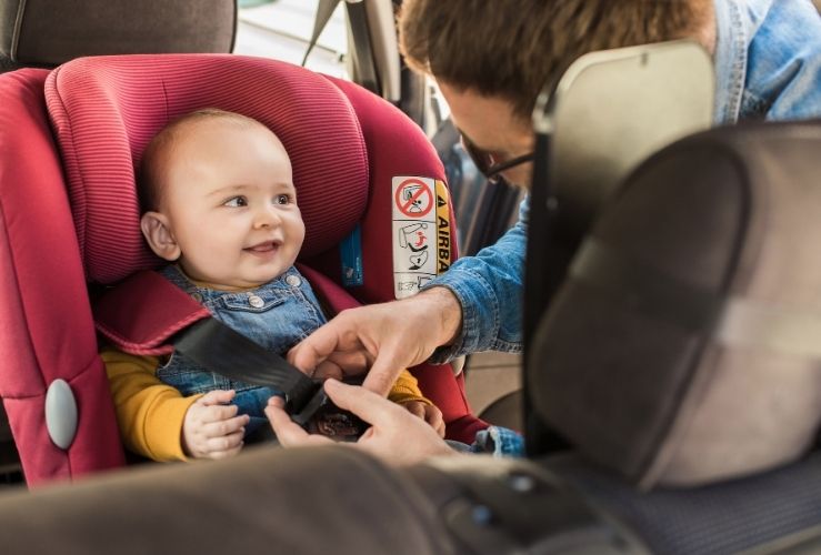 Young dad fixing baby into car seat