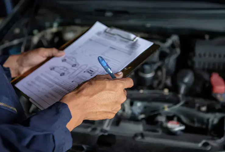 A person with a clipboard looking at a car's engine