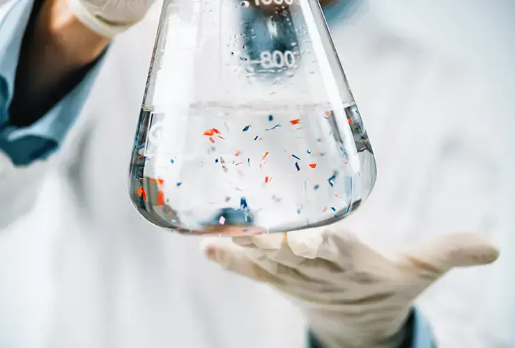 A scientist holding a flask containing microplastics
