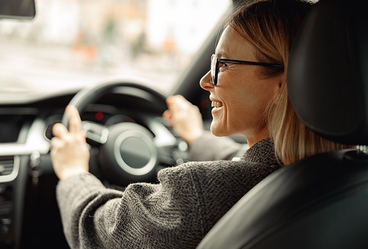 Smiling woman driving car and holding both hands on steering wheel