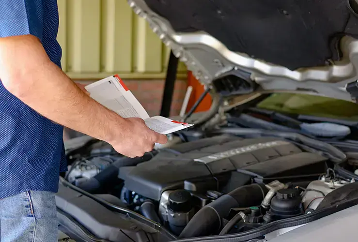 Person looking at car manual with the bonnet open