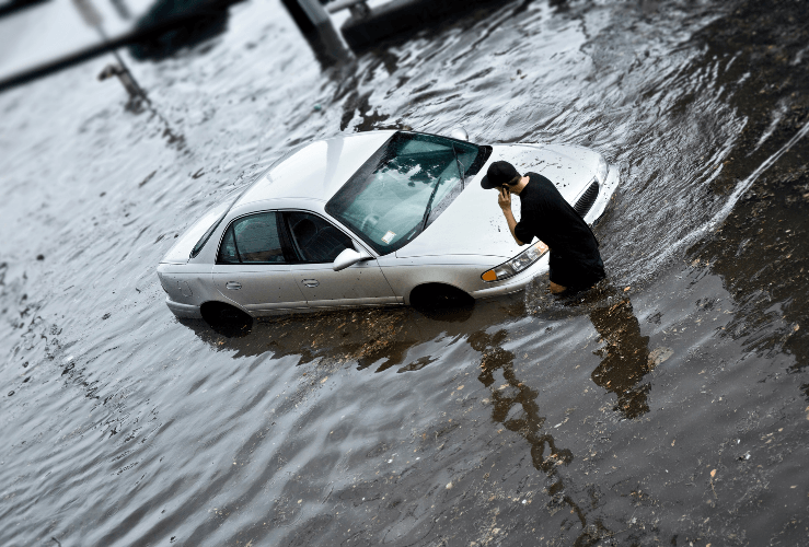 Man walking in flood water, having escaped hs flooded car