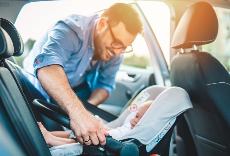 Dad fitting baby into child car seat